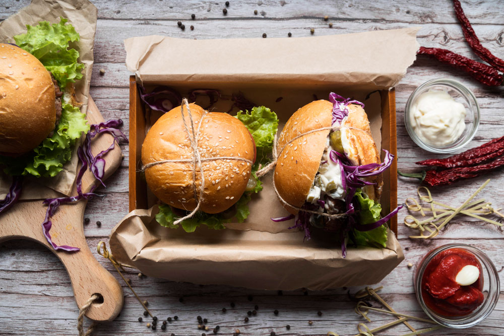 Zwei Burger mit Salat und Rotkohl liegen in einer Box, daneben stehen Schälchen mit Ketchup und Mayonnaise.